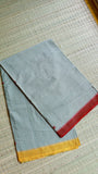 Top-down view of a folded Dhonekhali cotton saree on a textured mat, displaying the contrasting yellow and red temple borders.
