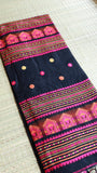 Close-up fold of the pallu section of a black Baluchari cotton saree, displaying dense rows of magenta, orange, and golden temple-inspired architectural thread work.