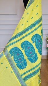 Close-up of the lemon yellow Baluchari cotton saree pallu draped vertically, highlighting the large, intricate teal blue paisley motifs and magenta pink details.