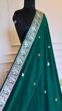 A detailed shot focusing on the silver temple-motif border and delicate gold and silver butis woven into the body of the emerald green cotton fabric