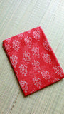 A neatly folded red Handblock Bagru printed Kota Doria cotton saree with matching blouse piece fabric, displayed flat on a natural woven grass mat.