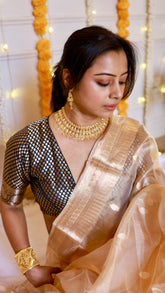 Close-up detail shot showing the rich woven zari pallu border of the metallic gold tissue silk saree and contrasting dark brocade blouse.