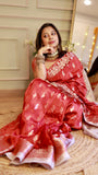 Model seated comfortably on a woven rug showcasing the relaxed fit, elegant pallu fall, and traditional Indian styling of the red Banarasi saree.