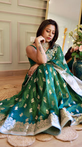 Full shot of a woman in an emerald green silver zari Banarasi georgette saree seated on a woven rug.