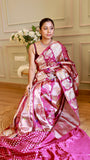 Front view of model seated on a stool wearing a magenta Munga Banarasi saree with silver zari Kalash motifs and a silver choker necklace.
