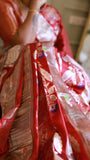 Close-up macro shot highlighting the fine weave, silver zari threadwork, and subtle color accents on the red Munga Banarasi saree pleats.