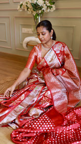 Seated pose displaying the pleats and intricate silver zari border of the red Munga Banarasi saree paired with a brocade blouse.