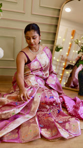 Model sitting comfortably to showcase the soft drape and fan pleats of the pink Banarasi silk saree.