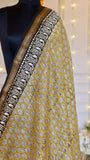 Close-up view of mustard yellow Maheshwari silk saree fabric showing detailed leaf block print and woven metallic zari edge.