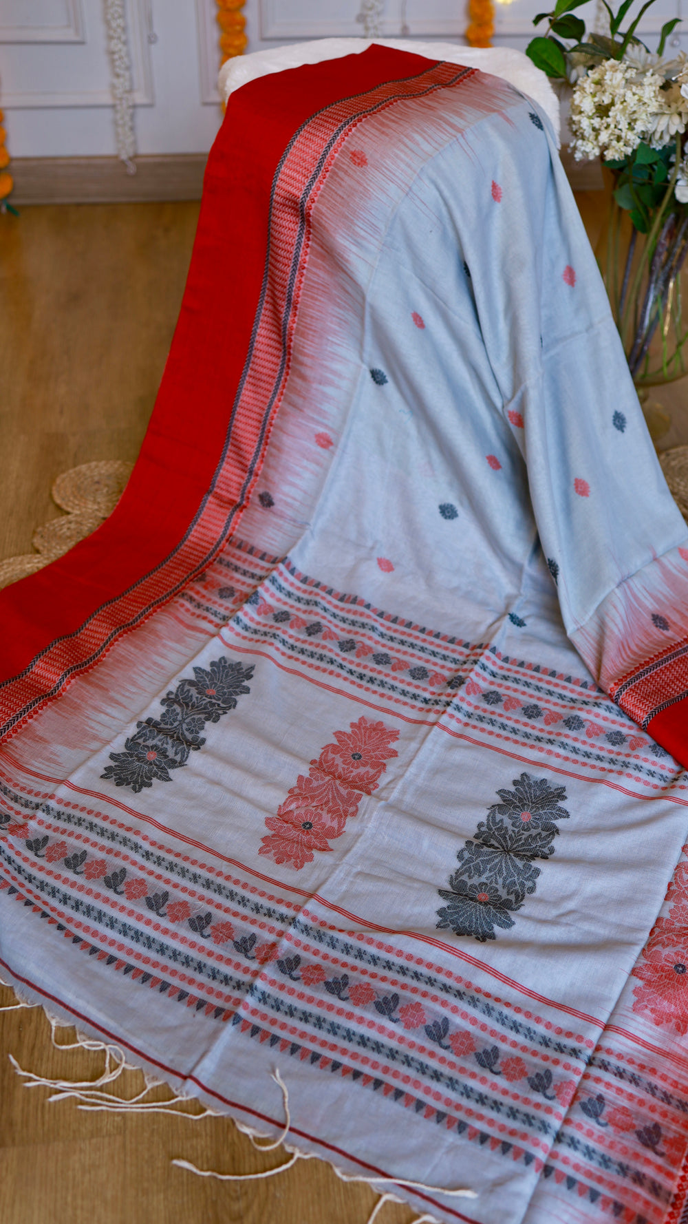 Intricately woven pallu of the off-white cotton Bomkai saree displaying dark grey and red floral extra-weft motifs and traditional geometric border lines