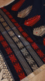 Detail shot showing the woven geometry border, crimson motifs, and tassel edging of the handwoven khadi saree.