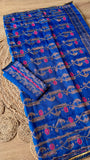 Close-up of Royal Blue Kardana Jamdani Saree pallu showing intricate pink floral hand-embroidery, kardana beadwork vines, and the folded matching blouse piece on a jute mat background.