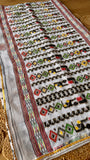 Off-white Kardana Jamdani saree featuring elaborate geometric diamond motifs in red, yellow, and green hand-embroidery along the pallu.