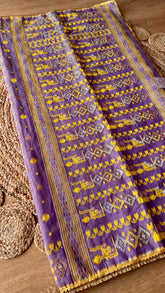 Close-up of handwoven lavender Kardana Jamdani saree pallu featuring mustard yellow motifs, glass beadwork, and mirror embellishments on a woven jute mat background.
