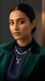 Woman wearing a green blazer and dark top with jewelry, against a dark background.