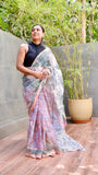 Woman wearing a Elegant hand-block printed pastel pink Kota Doria Cotton saree with a gold border, paired with a black sleeveless high-neck blouse and silver jhumka earrings.