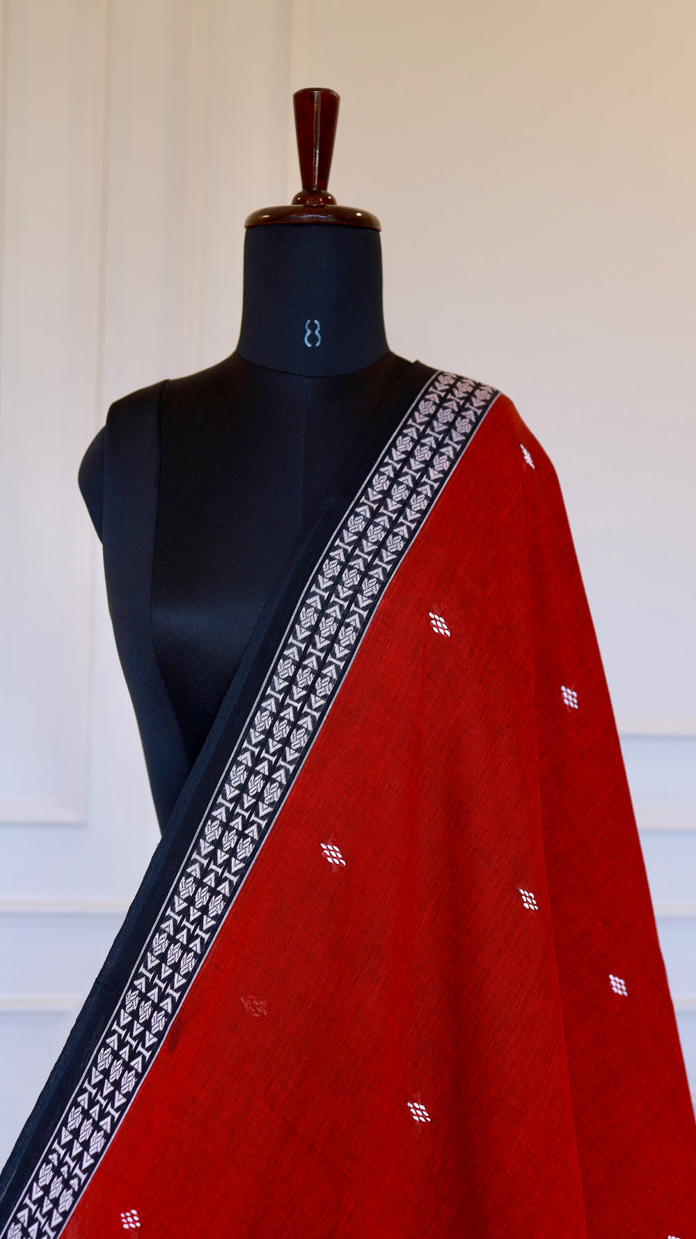 Close-up of the black border on the red Dhonekhali saree highlighting the intricate white geometric hand-thread embroidery.