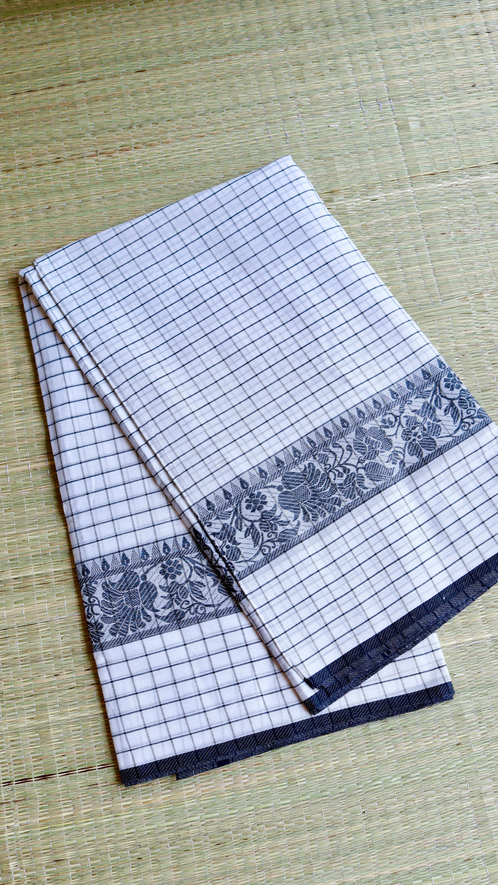 Neatly folded Dhonekhali handloom cotton saree showing texture and
thread work detail.