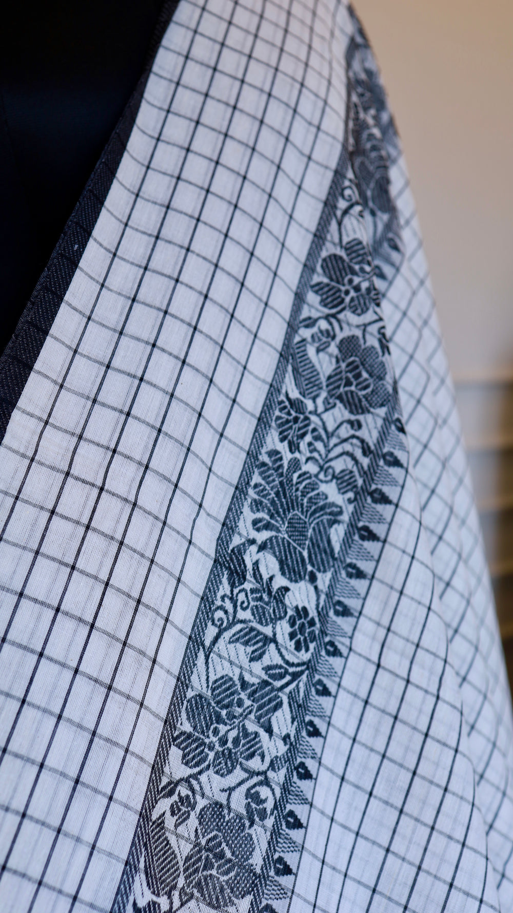 Close-up of the intricate black floral thread work border on a white
cotton saree.