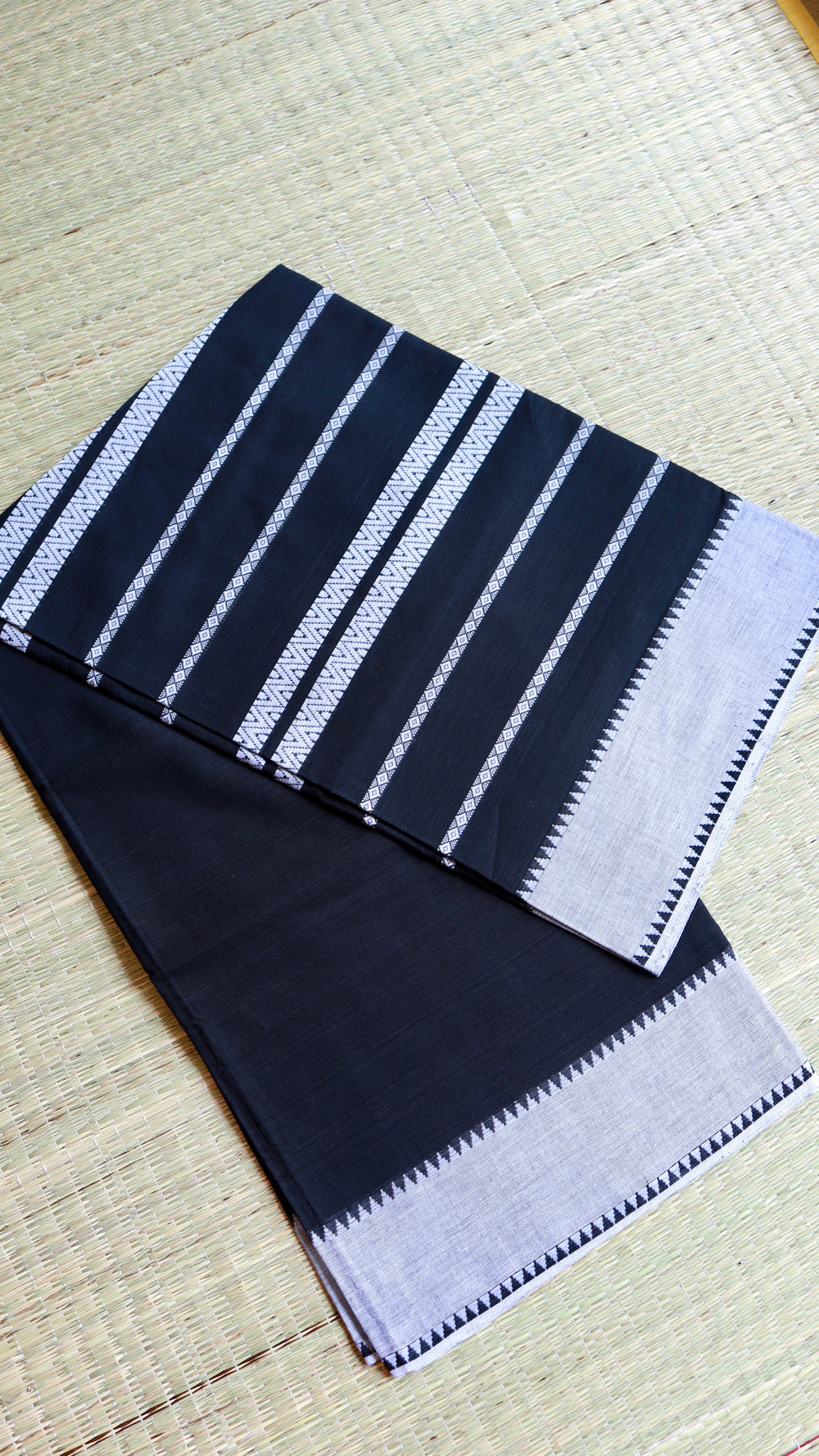 A neatly folded Black Dhonekhali Handloom Cotton Saree on a traditional mat showing the white thread work patterns.