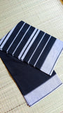 A neatly folded Black Dhonekhali Handloom Cotton Saree on a traditional mat showing the white thread work patterns.