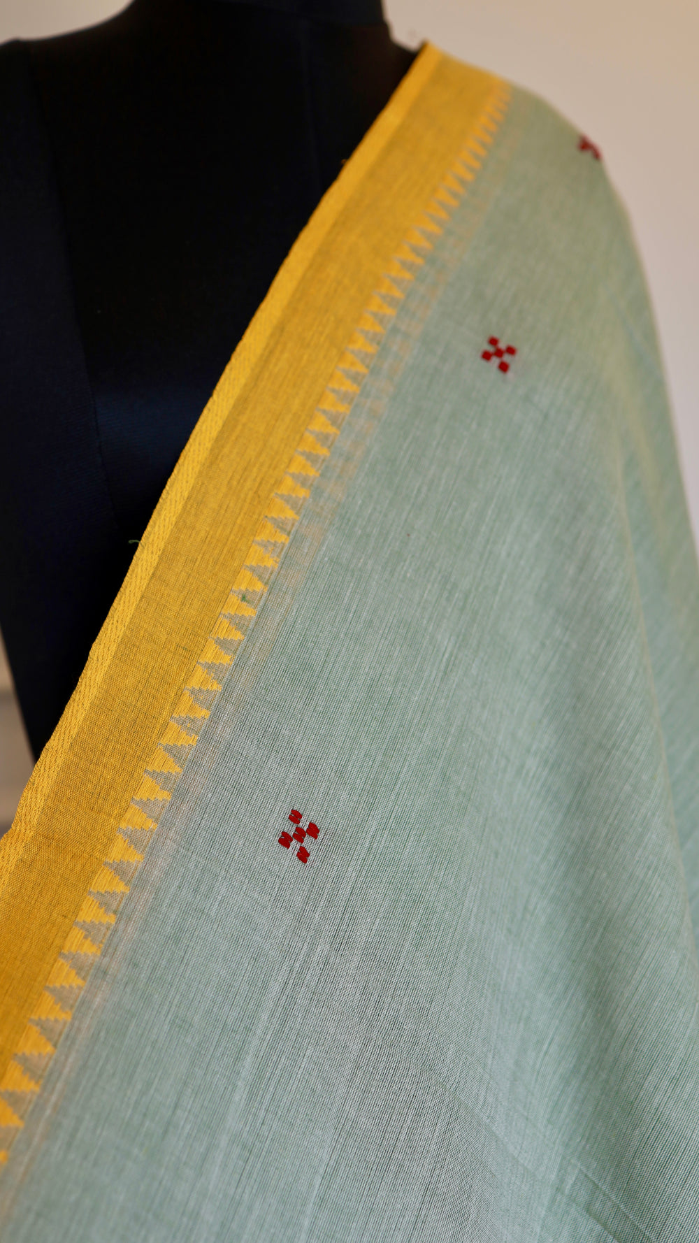 Close-up of the yellow border on a sage green handloom saree, highlighting the fine weave and small red embroidered motifs.