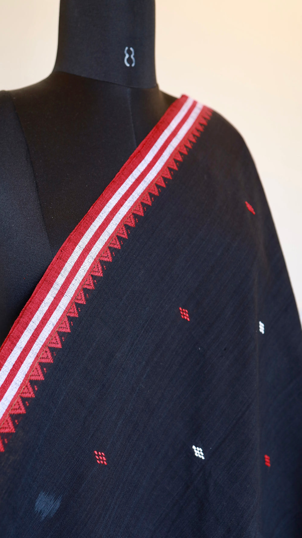 Close-up shot of the hand-woven red serrated border and intricate white diamond motifs on Dhonekhali cotton fabric