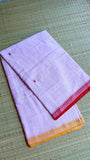 Folded Dhonekhali cotton saree on a grass mat highlighting the dual-toned red and mustard borders.