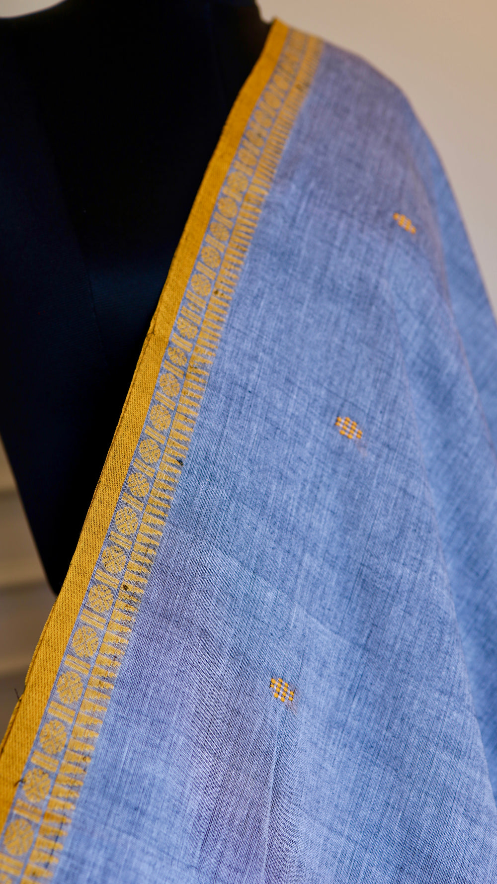 Extreme close-up of the ochre yellow border and intricate thread work on a steel blue Bengal handloom cotton saree.