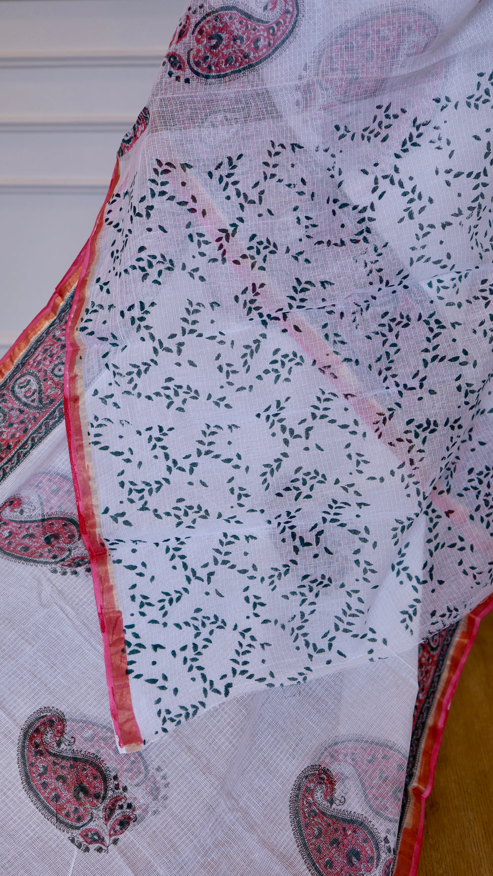 Close-up of the semi-transparent texture of a white Kota Doria pure cotton saree, showing a delicate pattern of small green hand-printed leaves.
