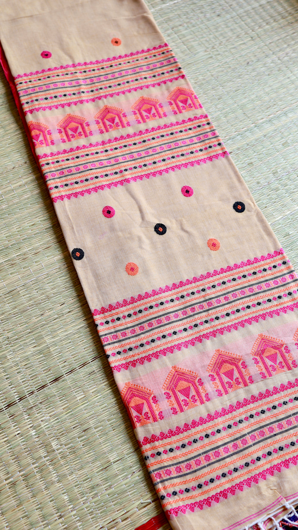 A flat-lay view showing the neatly folded pallu of the beige Baluchari cotton saree, showcasing detailed rows of pink temple-style house motifs and multi-colored threads.