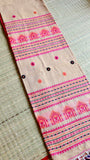 A flat-lay view showing the neatly folded pallu of the beige Baluchari cotton saree, showcasing detailed rows of pink temple-style house motifs and multi-colored threads.