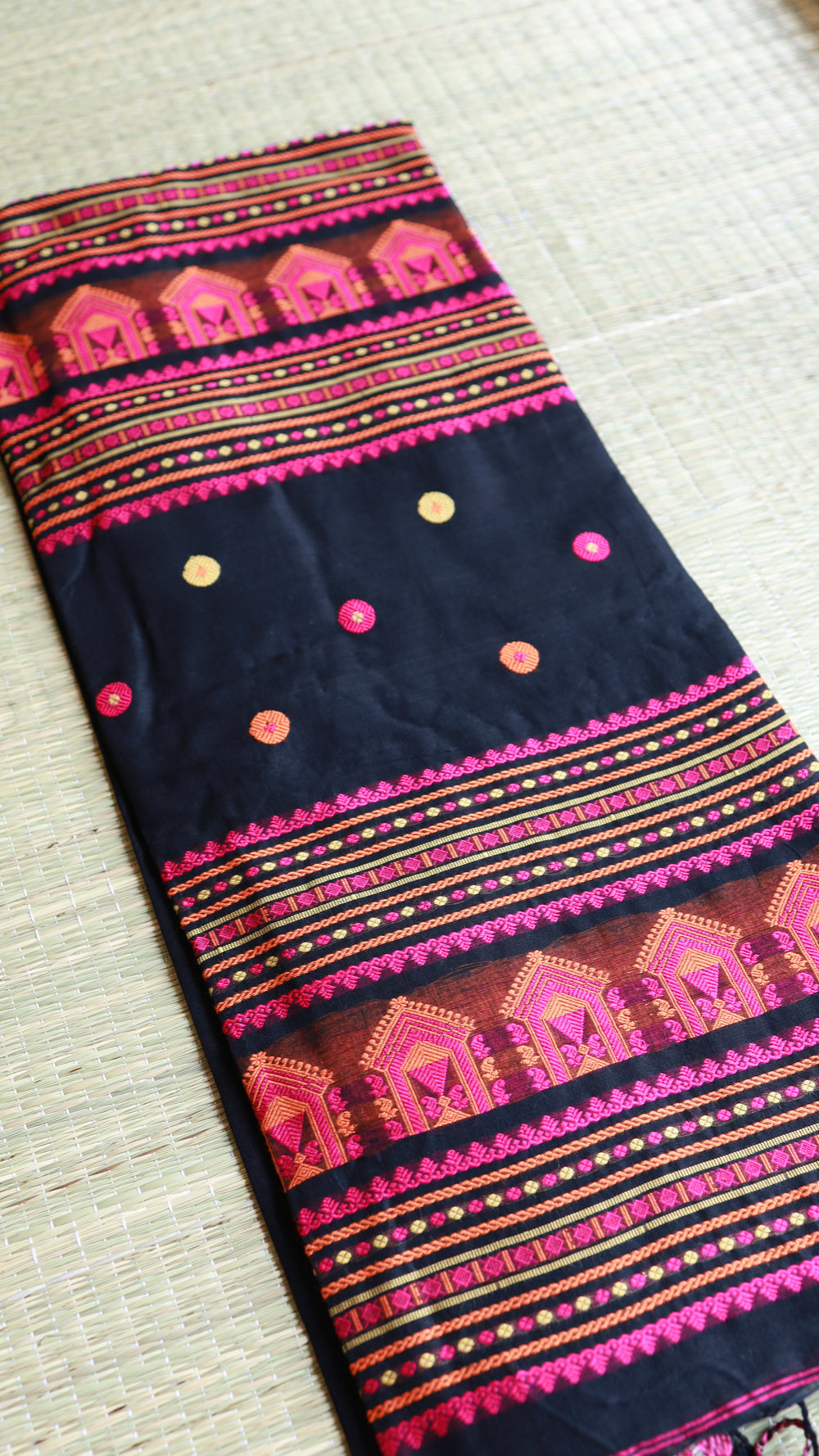 Close-up fold of the pallu section of a black Baluchari cotton saree, displaying dense rows of magenta, orange, and golden temple-inspired architectural thread work.