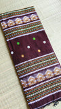 Flat-lay view of a folded coffee brown Baluchari cotton saree showing the stacked horizontal temple motifs on the pallu and the multicolored geometric borders.