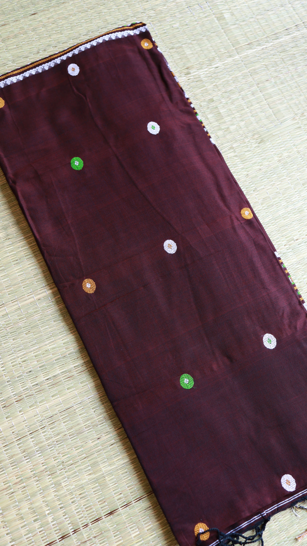 Top-down close-up view of the folded coffee brown saree body highlighting the scattered white, green, and gold circular buttas on the premium woven fabric texture.