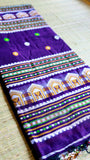 Close-up of a neatly folded deep purple Baluchari cotton saree showcasing the intricate white and golden-mustard traditional hut motifs on the border.