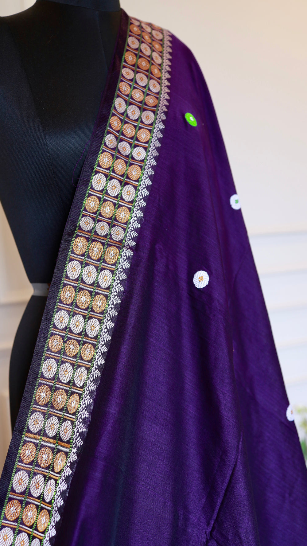 Detailed close-up shot of the multi-colored geometric border and circle motifs on the deep purple Baluchari cotton saree, displaying the expert craftsmanship.