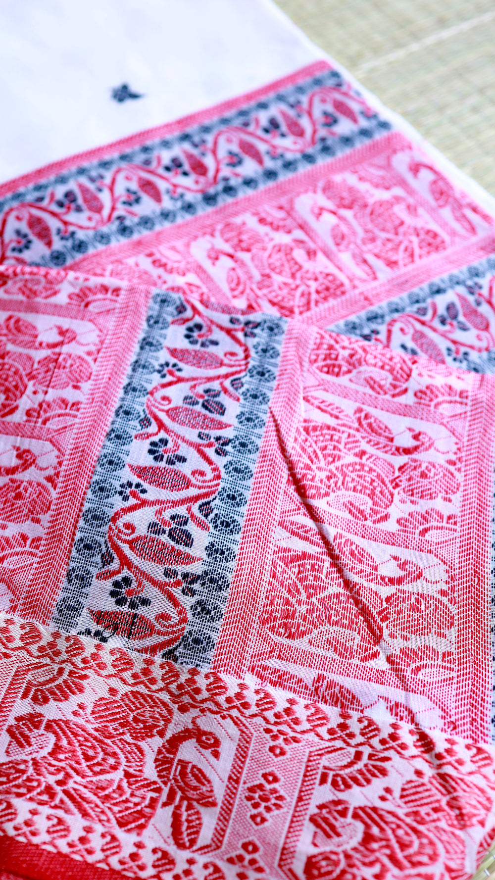 Detailed view of the expansive saree pallu featuring horizontal rows of traditional handwoven red and black motifs on a premium cotton base.