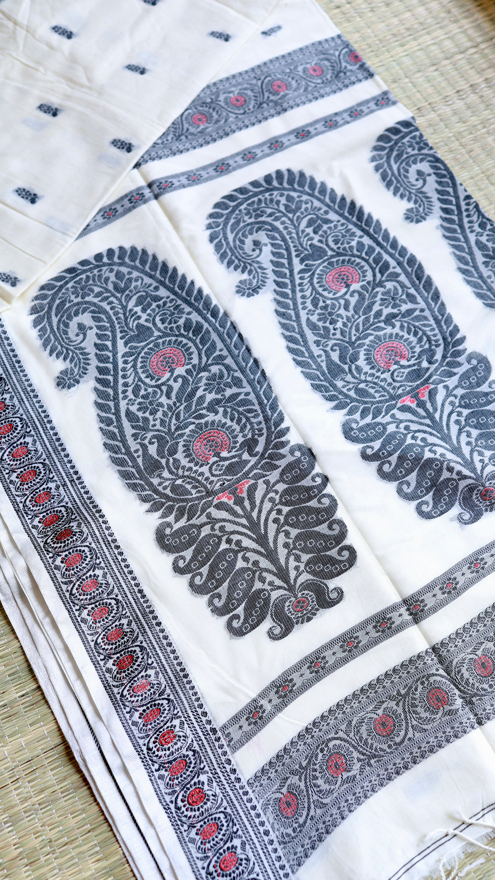 Flat lay presentation of the off-white Baluchari Cotton Saree showing the contrast between the minimalist body butis and the heavy paisley pallu.