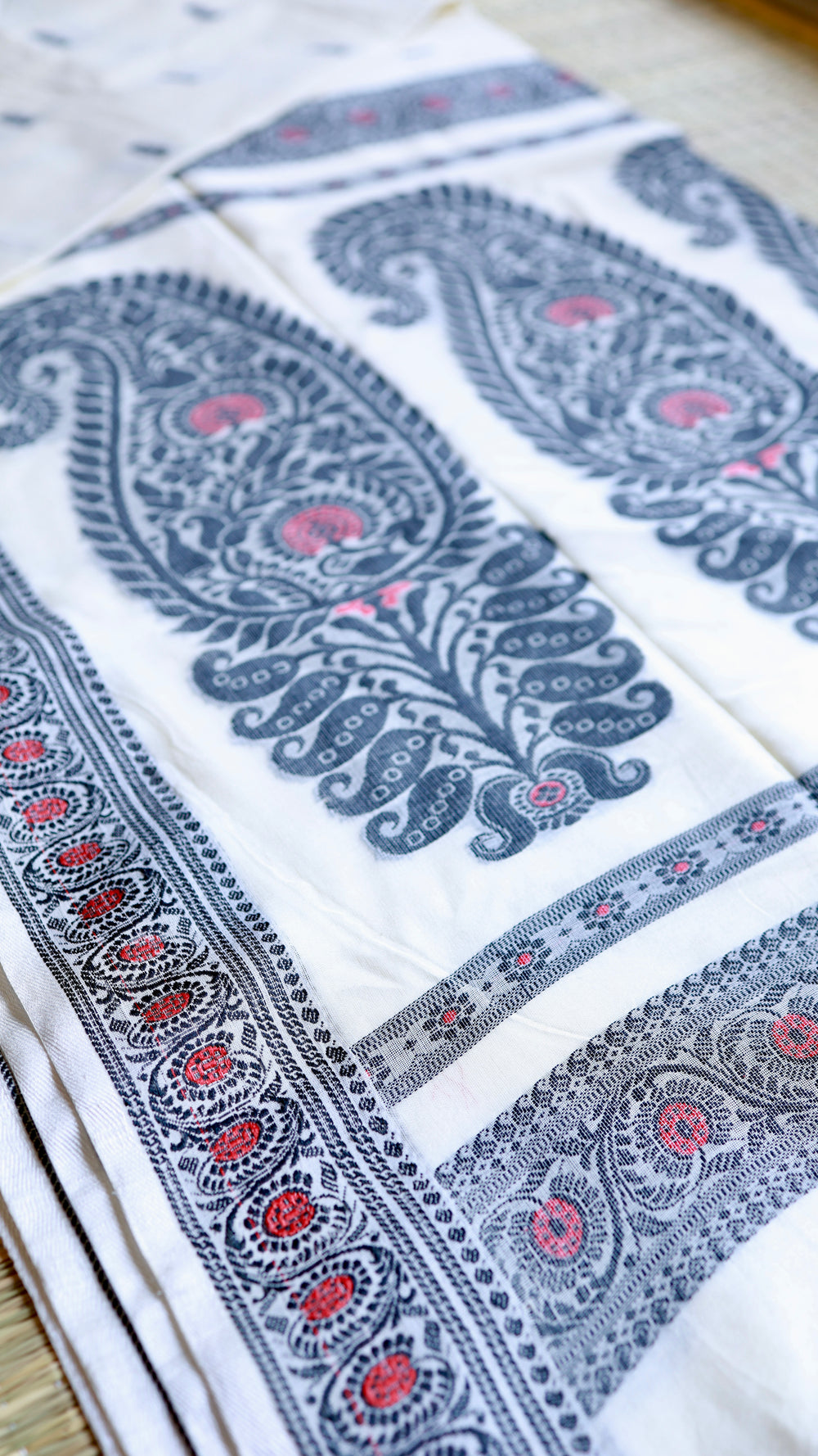 Detailed macro shot of the woven black border and red floral geometric patterns of the Baluchari Cotton Saree on a flat surface.