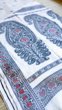 Detailed macro shot of the woven black border and red floral geometric patterns of the Baluchari Cotton Saree on a flat surface.