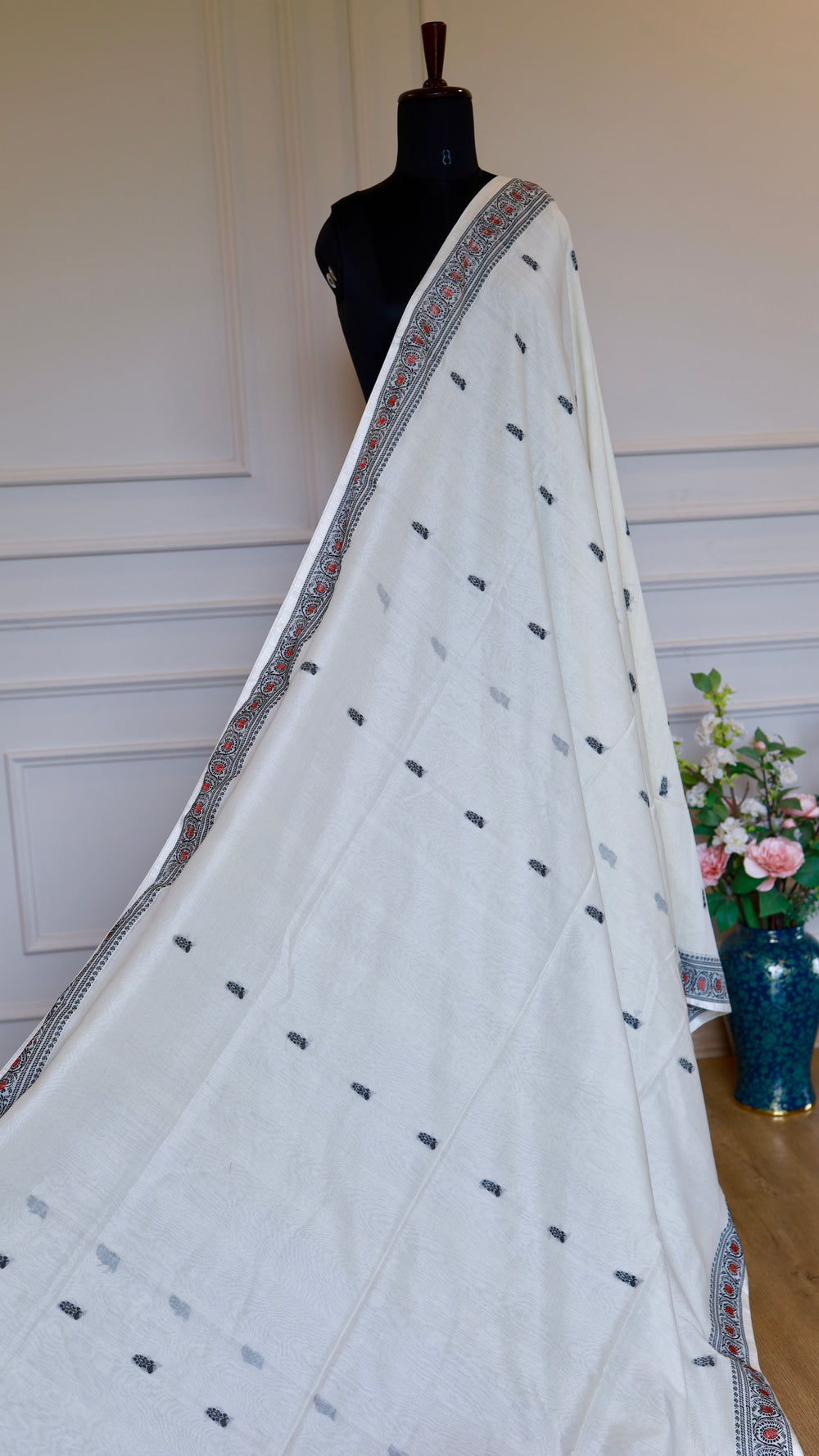 Full-length elegant drape of the off-white Baluchari Cotton Saree on a black mannequin, showcasing its graceful fall and scatter buti design in a beautifully lit room.