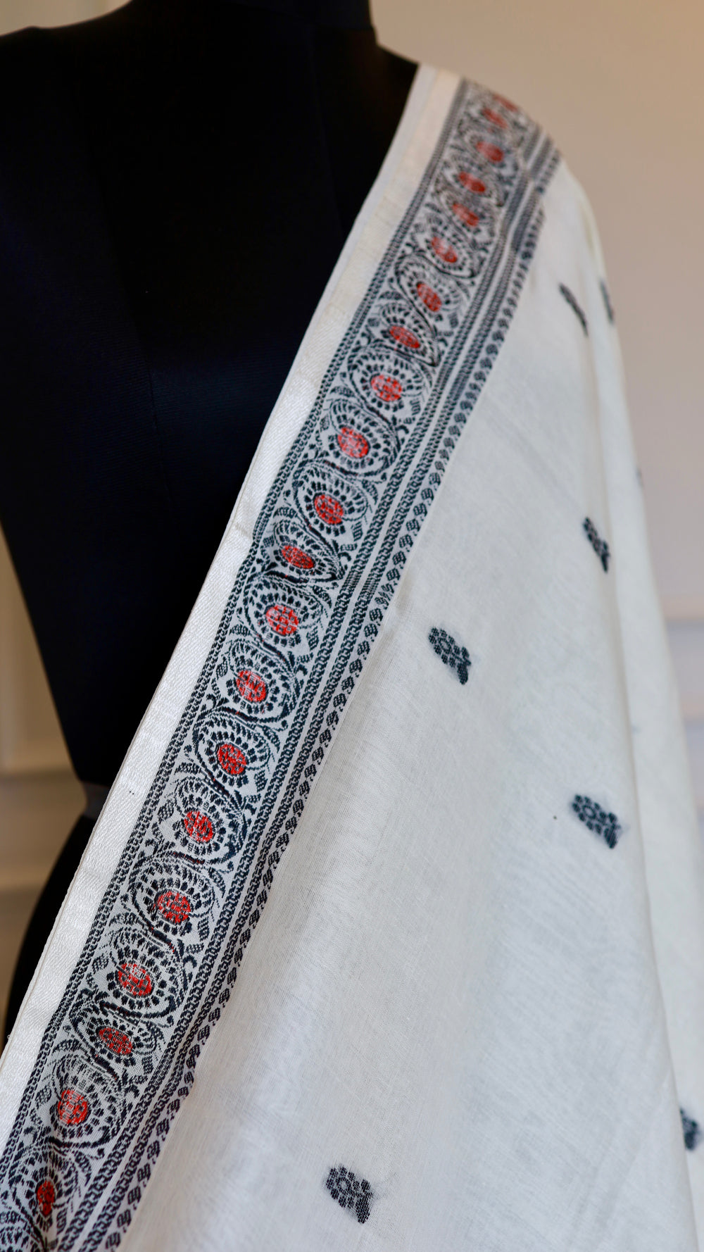 A perspective view of the Baluchari Cotton Saree draped on a mannequin, highlighting the intricate black and crimson running border against the off-white fabric.