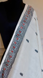 A perspective view of the Baluchari Cotton Saree draped on a mannequin, highlighting the intricate black and crimson running border against the off-white fabric.