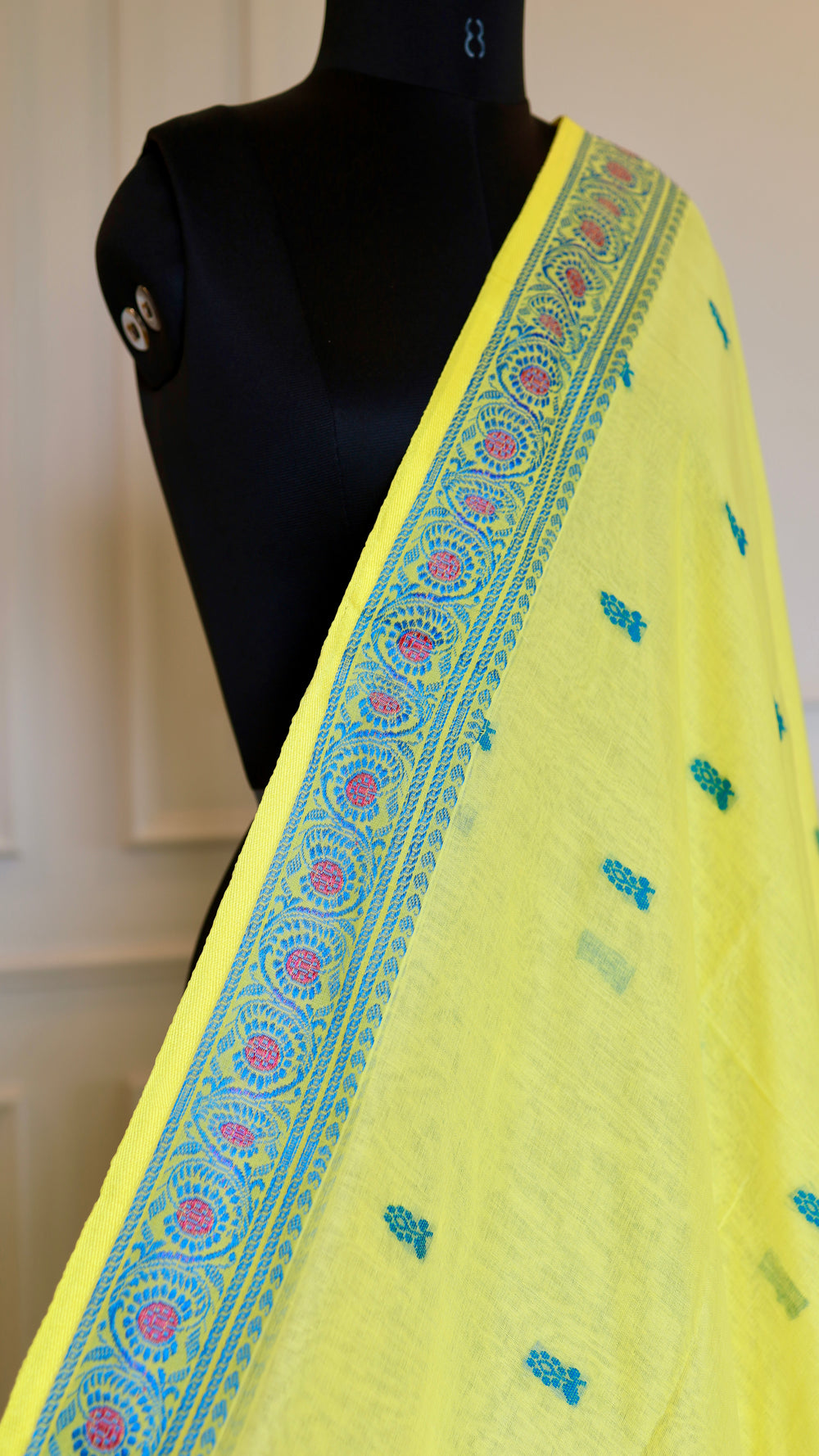 Detailed macro shot of the saree shoulder drape on a mannequin, focusing on the intricate blue and pink circular patterns along the handwoven border.