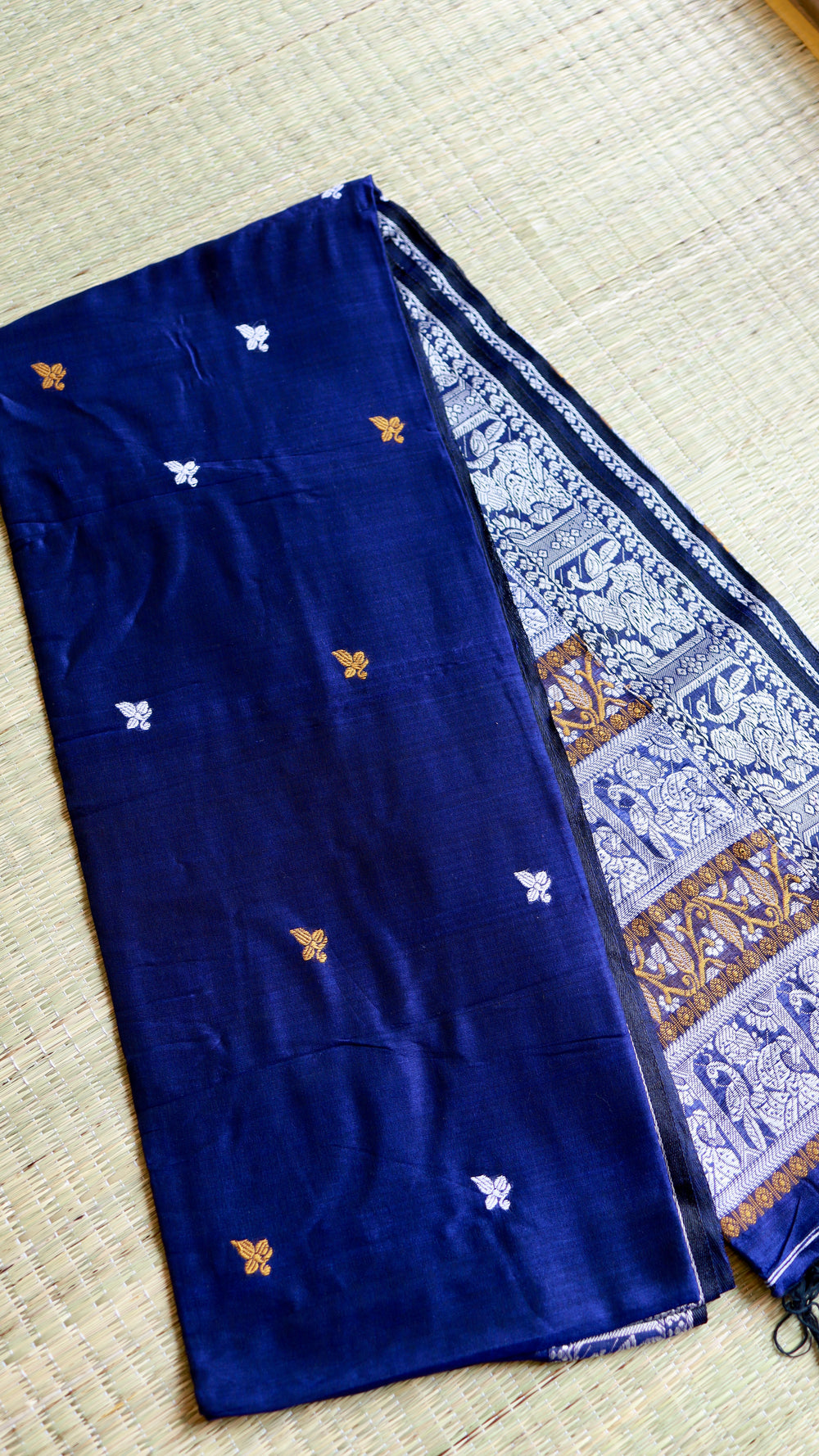 A flat-lay presentation of the royal blue Baluchari Cotton Saree neatly folded on a mat, cleanly showing the distribution of small embroidered motifs alongside the decorated pallu edge.