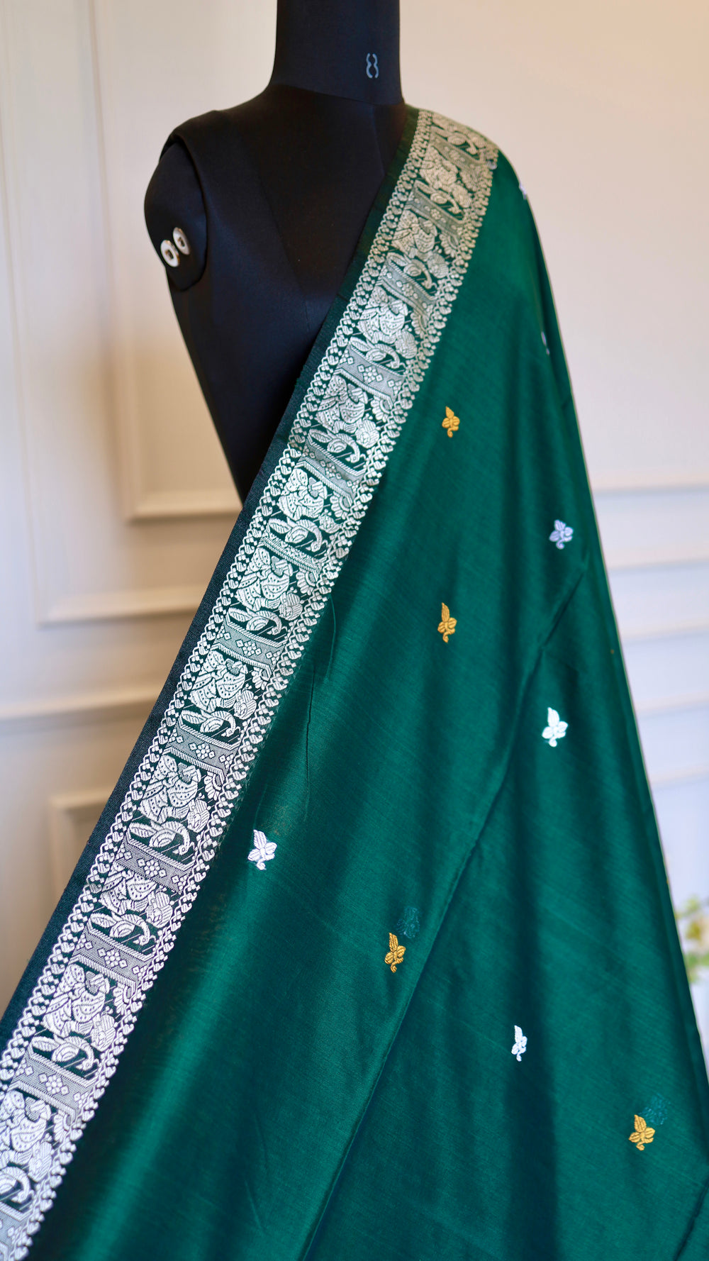 A detailed shot focusing on the silver temple-motif border and delicate gold and silver butis woven into the body of the emerald green cotton fabric