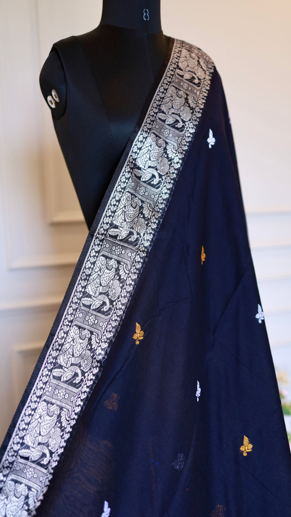 Close-up view of the midnight black Baluchari cotton saree on a mannequin, showcasing the intricate silver border woven with traditional mythological motifs and gold butis.