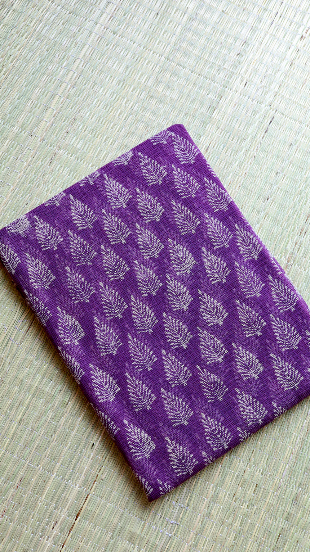Neat flat-lay fold of the premium purple cotton fabric on a woven mat, showcasing the dense, uniform leaf-cluster handblock prints.