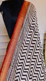 Close-up shot of a Handblock Printed Maheshwari Silk Saree draped on a mannequin, showcasing the crisp black and white chevron pattern alongside a detailed red and gold woven zari border.